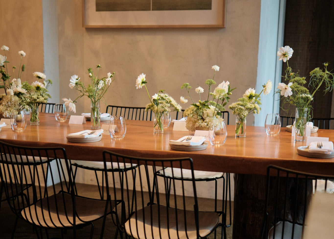 Dining room with a long wooden table set for a meal, featuring chairs and floral arrangements.