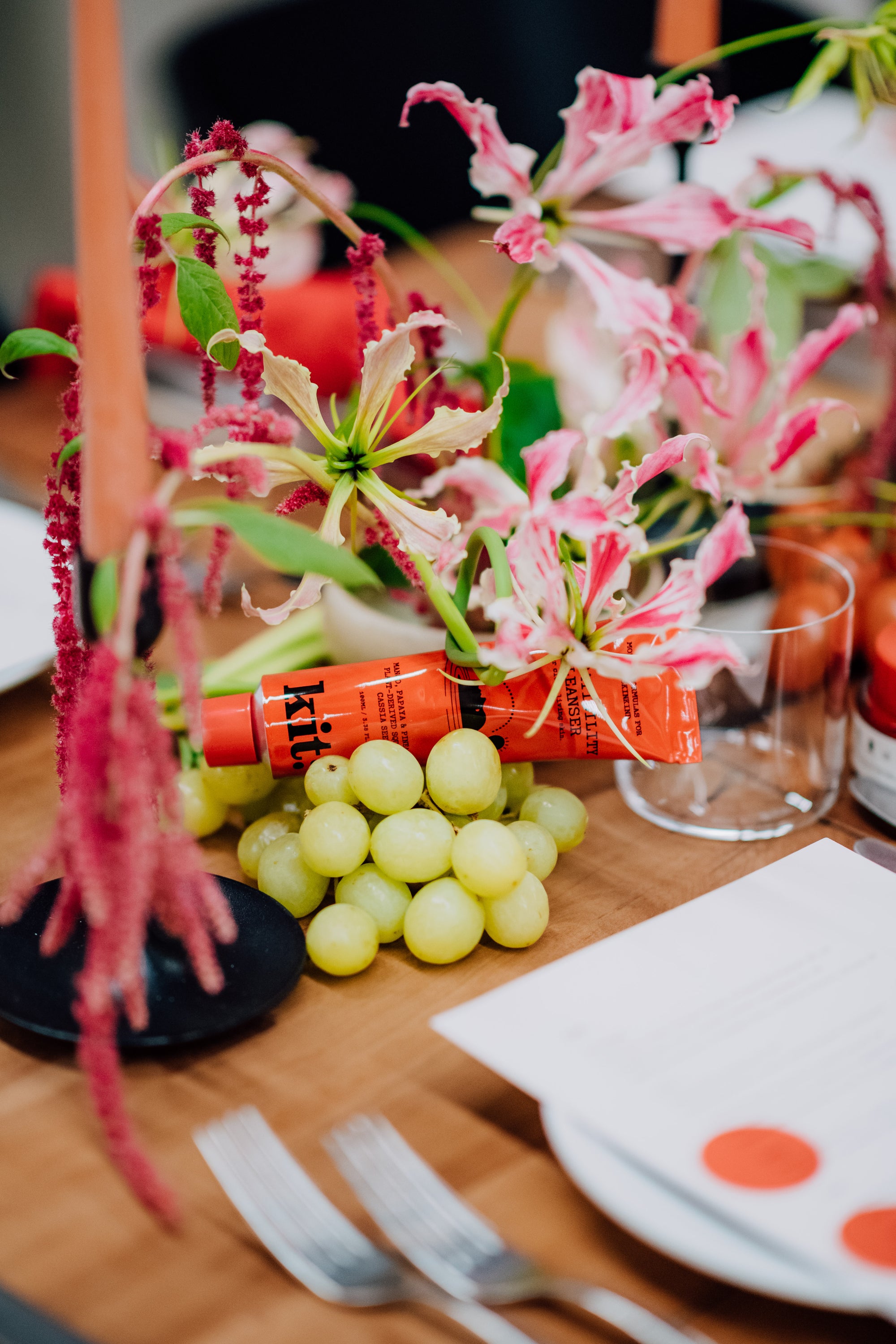 Decorative table setting with flowers, grapes, and cutlery on a wooden surface. Displaying Kit Skincare.
