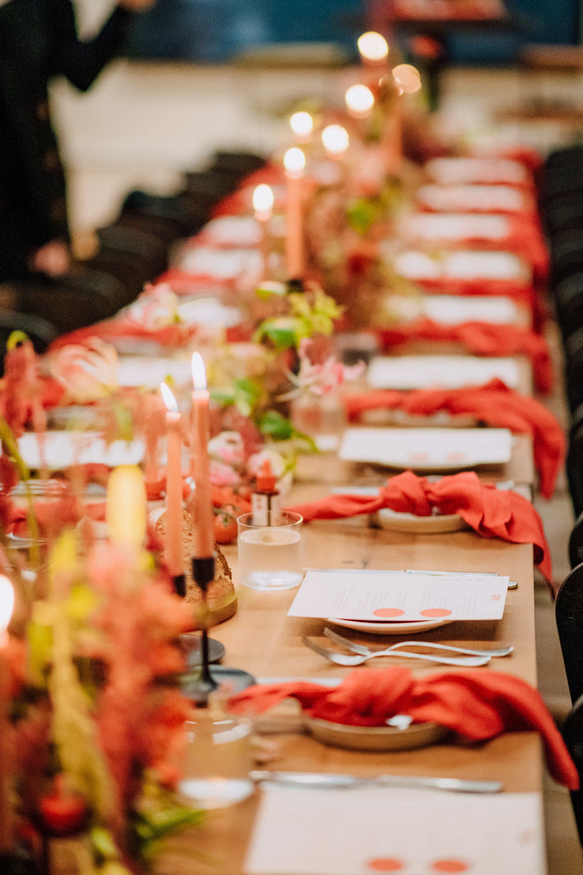 Long table set for a formal dinner with red napkins, candles, and many florals.