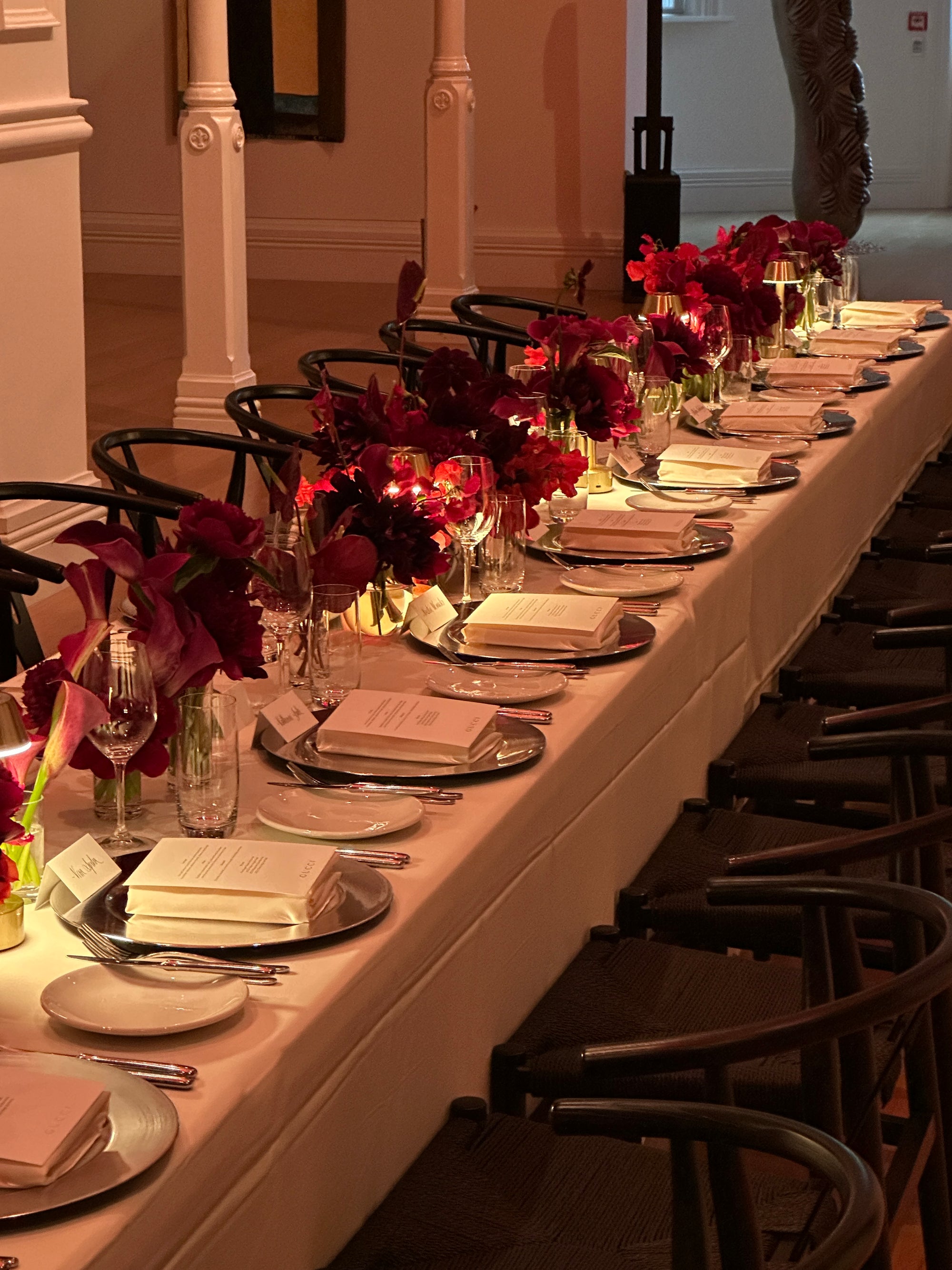 Long table set for a formal event for Gucci with red floral centerpieces, plates, and glasses.