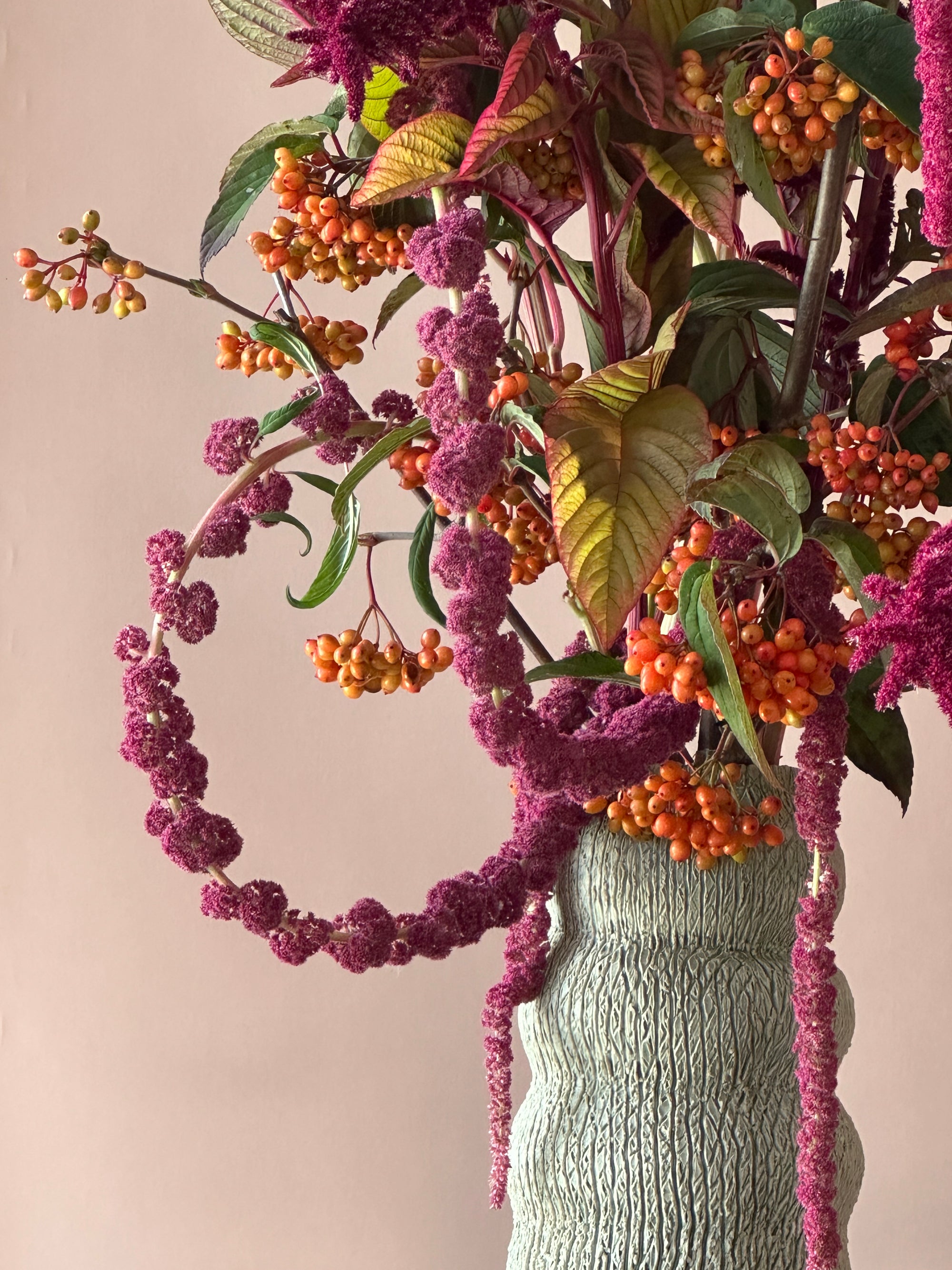 Fresh floral arrangement with burgundy flowers and orange berries in a handmade green vase on a beige background