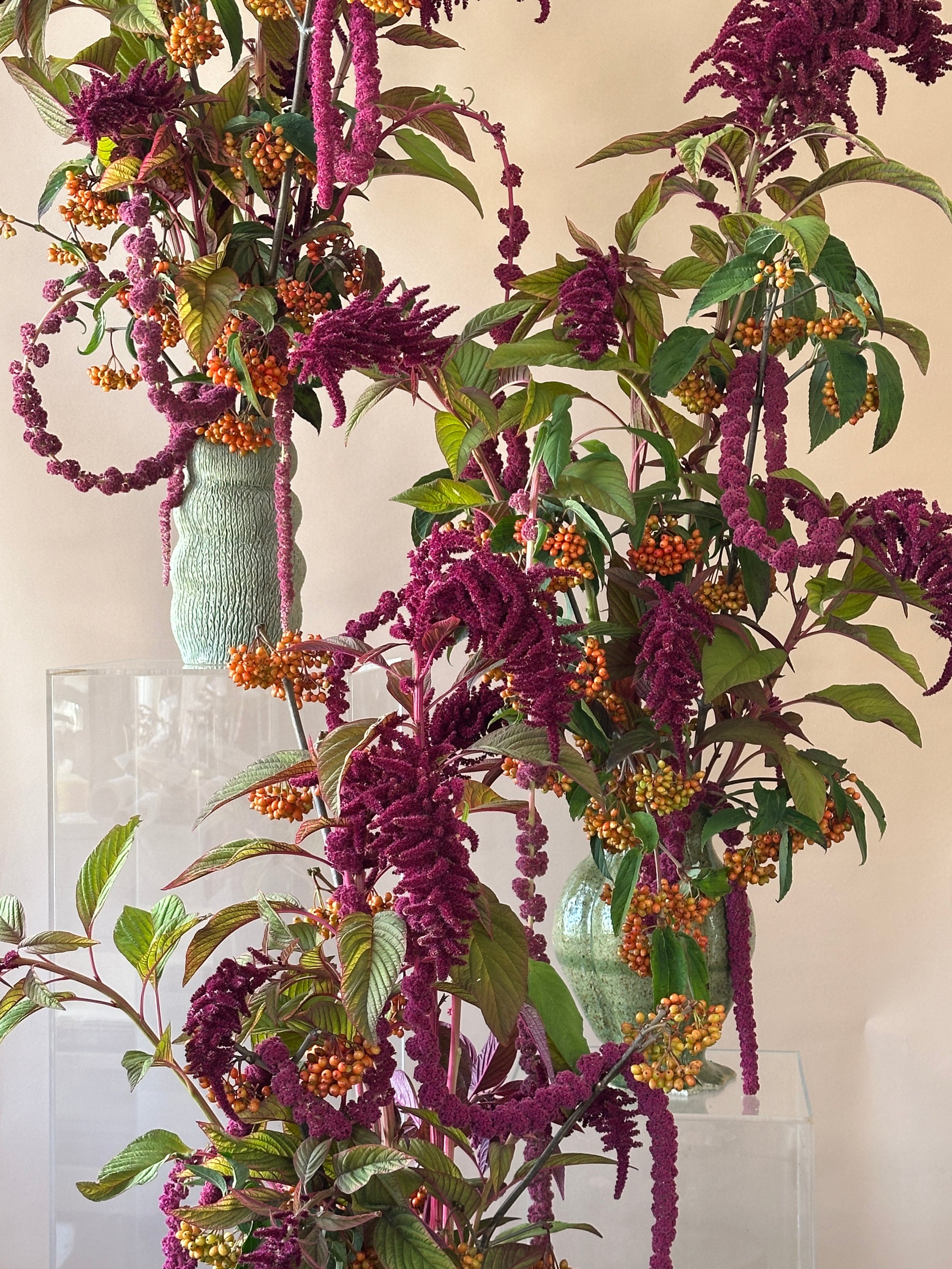 Decorative floral arrangements with burgundy and green leaves and orange berries on a beige background