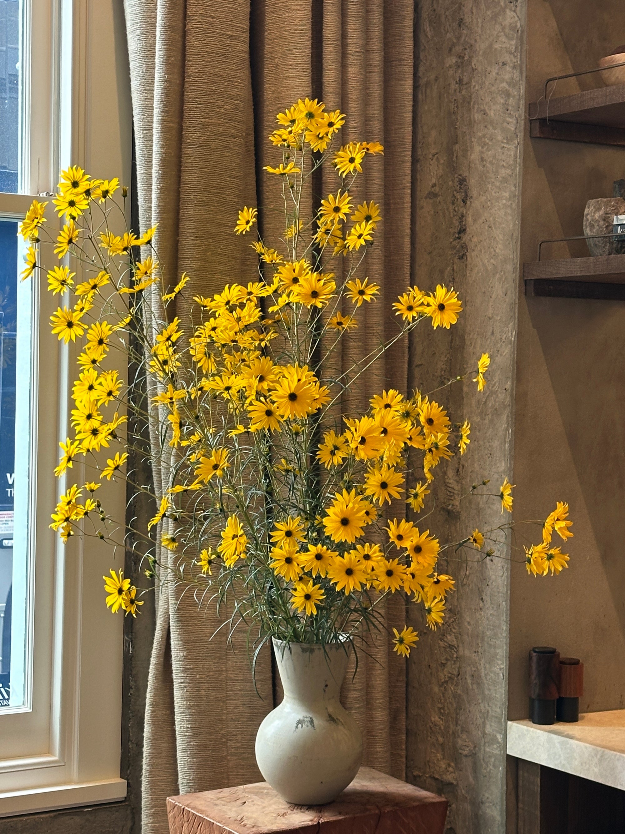 Yellow flowers on a wooden surface with a vase in the background