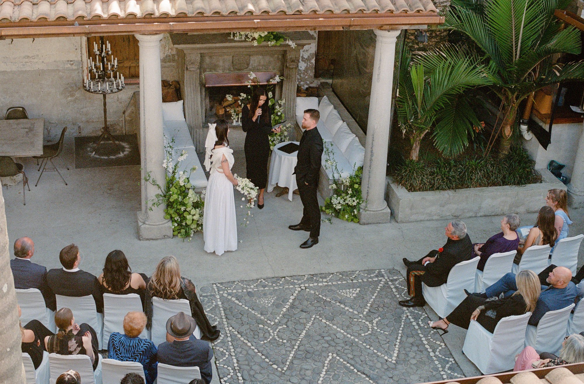 Wedding ceremony taking place in an outdoor setting with guests seated on chairs.