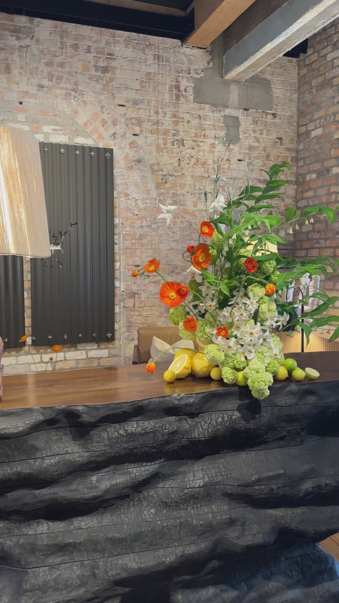 A large display of whites, green and orange flowers including poppies and snowball. Fresh lemons cut in half and placed around the base in a cluster.