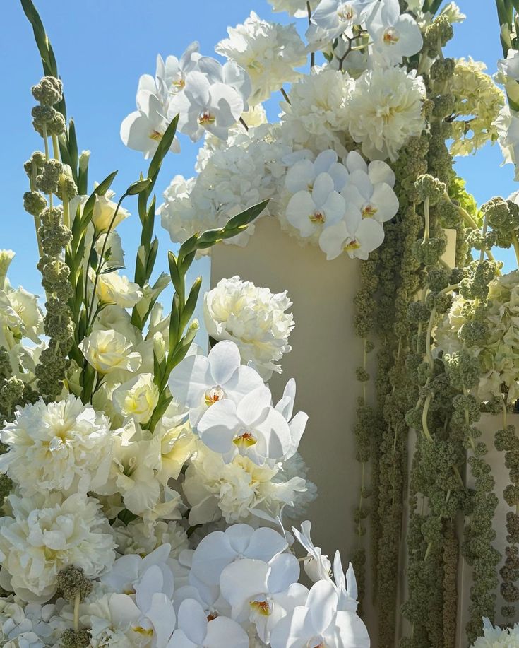 Floral arrangement with white flowers and greenery against a blue sky.